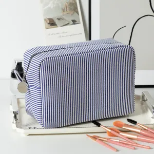 Close-up view of a blue and white striped seersucker makeup bag with pink brushes.