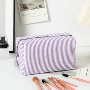 Detailansicht der lila gestreiften Seersucker-Kosmetiktasche mit Reißverschluss und Pinseln.
