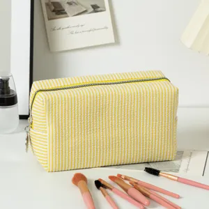 Große gelbe Seersucker-Kosmetiktasche mit Streifen, Kosmetik und Pinseln auf weißem Schreibtisch