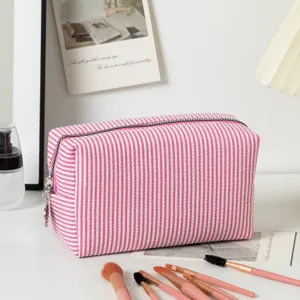 Seersucker gestreifte Kosmetikta-sche mit Make-up-Pinseln auf weißem Tisch