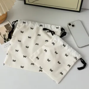 Set of two cream-colored cotton drawstring pouches featuring cute black bow patterns