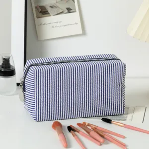 Detailansicht der gestreiften Seersucker-Kosmetiktasche mit Pinseln auf dem Tisch