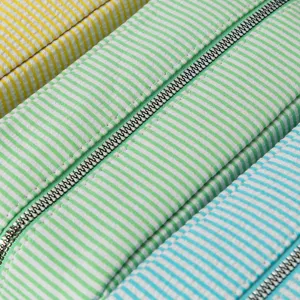 Detailed close-up showing the seersucker fabric and zipper of the striped cosmetic bag.