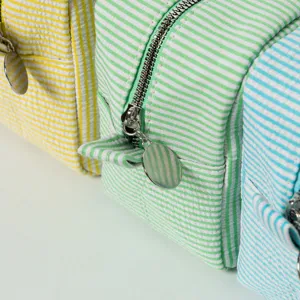 Macro detail view of seersucker striped cosmetic bags showing texture and metal zipper