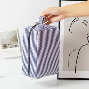 Blue striped seersucker travel cosmetic bag with portable handle shown held by hand