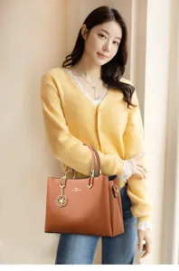 Elegant women brown leather handbag detail shot featuring stylish floral pendant and top handle.