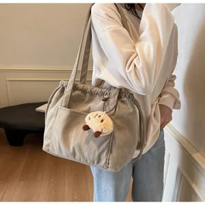Retro corduroy shoulder bag with drawstring and cute plush charm, casual large capacity tote.