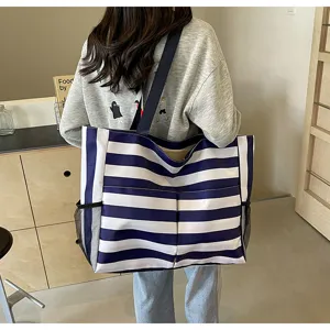 Große blau-weiß gestreifte Einkaufstasche mit Taschen, getragen von einem Modell im Café.