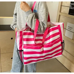 Große pink-weiß gestreifte Strandtasche, getragen von einem Modell in einer Freizeitkulisse.