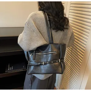 Detail view of a vintage black soft leather tote bag worn over a grey knit sweater