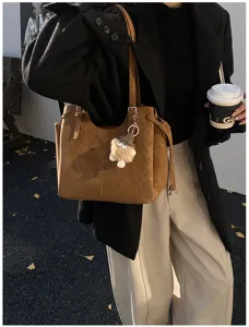 Detailed lifestyle shot of a large brown suede tote bag featuring a pom-pom charm