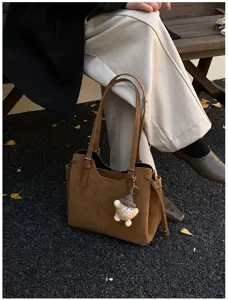 Detail shot of a soft caramel leather tote bag for women featuring a cute plush monster charm
