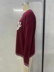 Side view detail of a wine red women's knit sweater with white letter embroidery and striped trim.