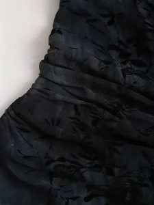 Détail de tissu mesh transparent noir montrant une texture de flocage en velours et motif floral.