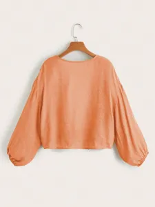 Detailansicht der eleganten orangefarbenen Langarmbluse mit Ballonärmeln und weichem Stoff.