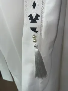 Detailed shot of white long robe with black embroidery, pearl beads, and elegant silver tassel.
