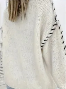 Detail view of women oversized knit sweater, white fabric with black contrast stitching.