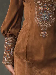 Vue en gros plan des détails de broderie exquis sur le poignet de la robe en suédine marron.