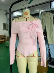 Dettaglio top in maglia con spalle scoperte, tessuto a costine rosa con fiocco in rete.