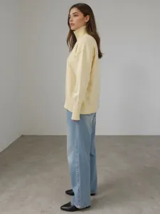 Détail de profil d'un pull jaune à col roulé ample et confortable assorti à un jean bleu.