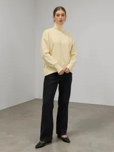 Pull col roulé ample jaune pâle assorti à un pantalon noir pour la saison automne hiver.