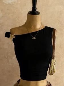 Primo piano dettagliato di un elegante crop top nero monospalla con spilla a stella.