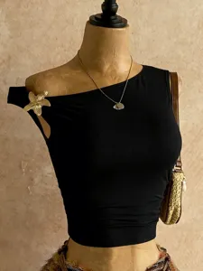 Vista dettagliata di un elegante crop top nero monospalla con spilla floreale dorata.