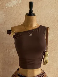 Primo piano di un crop top marrone monospalla con una spilla a forma di stella marina.