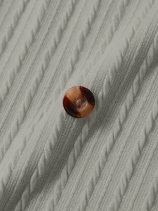 Close-up detail of cable knit sweater texture and tortoiseshell button, soft fabric view.