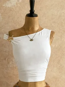 Top corto bianco monospalla con accessorio floreale dorato e collana elegante.