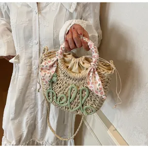 Detail view of a straw bucket bag with floral scarf handle and 'hello' embroidery.