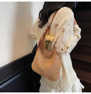 Detalle de bolso bandolera tejido con diseño calado de flores y adorno de borla.