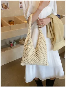 Woman carrying a beige handmade crochet hollow-out tote bag for summer beach outings.