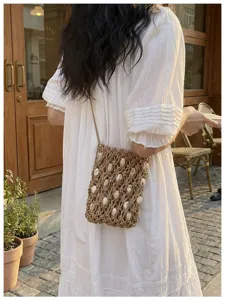 Close-up view of a handmade woven crossbody phone bag with shell beads over a white dress.