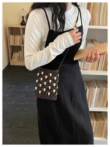 Detail view of a handmade woven phone bag with white bead accents in a library setting