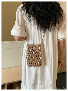 Back view of a boho woven crossbody phone bag with white bead accents on white dress