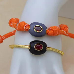 Détail en gros plan d'un bracelet entretoise ovale plaqué or 18k avec zircon rouge.