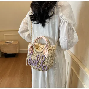 Detailed view of straw woven bucket bag with purple hello embroidery and floral ribbon