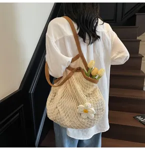 Detailed view of a cream mesh tote bag featuring brown straps and a white floral charm.