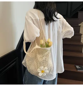 Detail of a cream crochet mesh tote bag with flower decor, carried over shoulder.