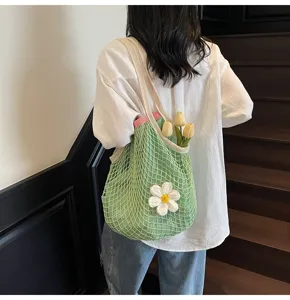 Lifestyle detail of a green crochet mesh tote bag decorated with a white flower charm