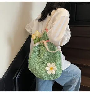 Detail view of a green mesh tote bag featuring a white crochet flower charm