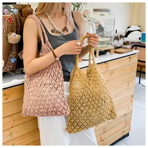 Model holding two colorful hand-woven macrame tote bags in a stylish cafe setting