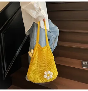 Yellow crochet mesh tote bag featuring a white flower charm shown on wooden stairs