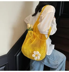 Stylish yellow hollow out mesh tote bag with a white flower charm on model shoulder