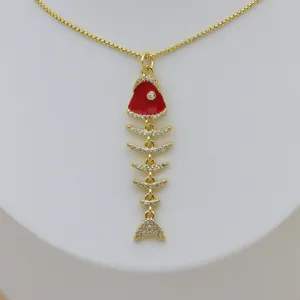 Detalle de colgante de espina de pescado dorado con esmalte rojo y circonitas