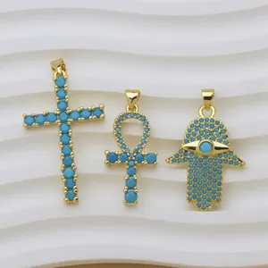 Vista macro detallada de colgantes chapados en oro con cruz, ankh y hamsa con piedras azules.