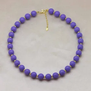Gros plan de détail sur le collier de perles rondes violettes avec espaceurs dorés et fermoir.