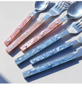 Close-up detail van roestvrijstalen bestekset met paarlmoer marmerroze en blauwe handgrepen.