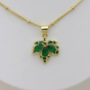 Close-up detail of a gold plated maple leaf necklace pendant adorned with sparkling green cubic zirconia.